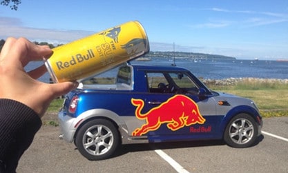 Person holding Red Bull can above a Red Bull mini car
